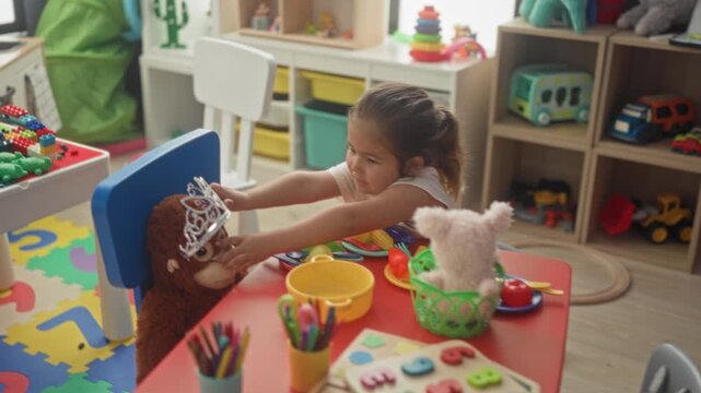 Hispanic girl reaches with both hands to place plastic tiara on a stuffed monkey at a playroom building; imaginative joy.