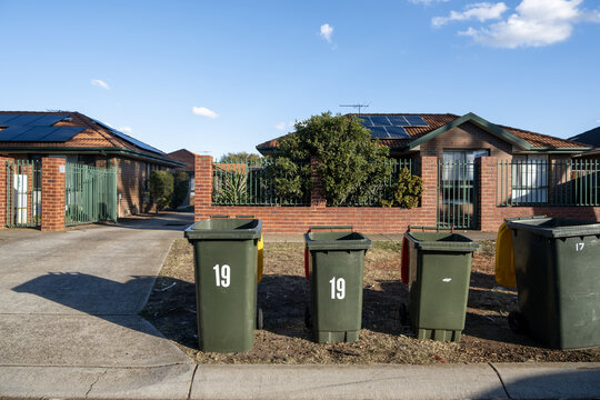 Wheelie bins line the footpath outside suburban homes or residential units in&nbsp; Melbourne Australia. Concept of waste collection, suburban infrastructure, and everyday Australian residential life.