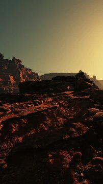 The scene shows a rocky landscape illuminated by the warm light of the setting sun. The sun casts long shadows on the ground, highlighting the textures of the rocks.