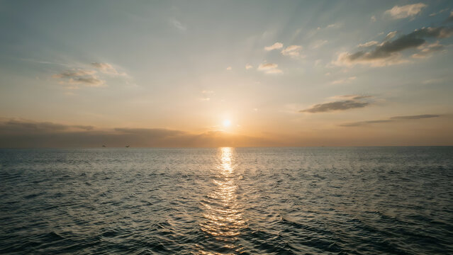 Golden sunset over calm ocean waters with soft clouds