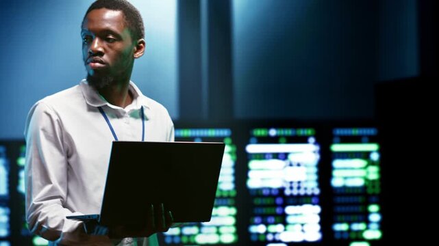 African American IT developer checks cybersecurity protections in a data center, reviewing access control during stalls server room firewalls.