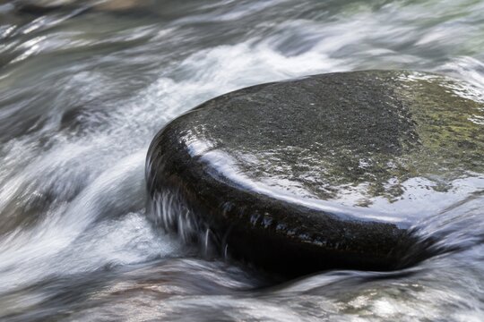 A fast-flowing stream smoothing the edge of a dark river rock, motion blur.