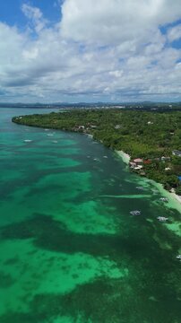 Vertical drone pulls back and ascends over Panglao, revealing turquoise reef flats, boats, shoreline, and inland areas of Bohol