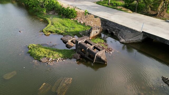 Aerial pullback of Igang Chapel Ruins in Virac, Catanduanes, showing shallow river water, a roadside bridge, and tropical village surroundings