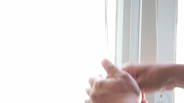 hand pulling a blind cord to open a window covering. Bright daylight enters the room, highlighting home comfort, privacy control, and modern interior design.