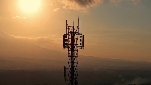 Communication antenna tower against golden hour sky, silhouette shot. Network, telecom, and wireless connectivity concept footage sunset.