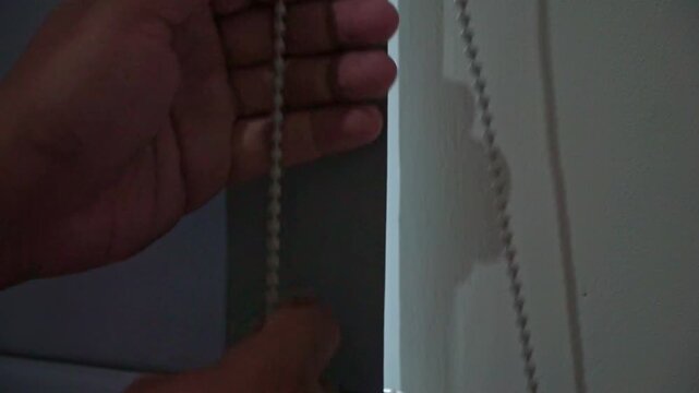 hand adjusting a roller curtain with a pull chain. Modern interior, sunlight management, and residential living concept.
