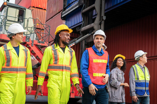 Diverse team of logistics workers and engineers at container terminal, industrial workers walking together at cargo shipping port, Group of team in safety gear inspecting shipping container yard