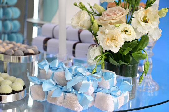 traditional bem casado wedding sweets with blue ribbon, wrapped party favors on elegant glass stand, baby shower sweet souvenir gift presentation, brazilian confection close up