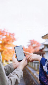 紅葉の街並みでスマートフォンの地図を確認する二人の旅行者の手元