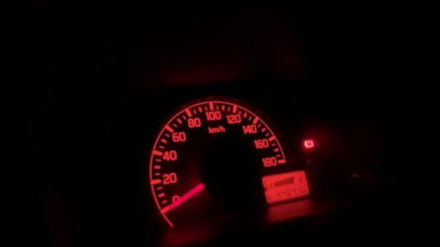 Close up of a car's dashboard in darkness, featuring a speedometer  and The illuminated warning. symbols create a moody, nighttime driving ambiance.