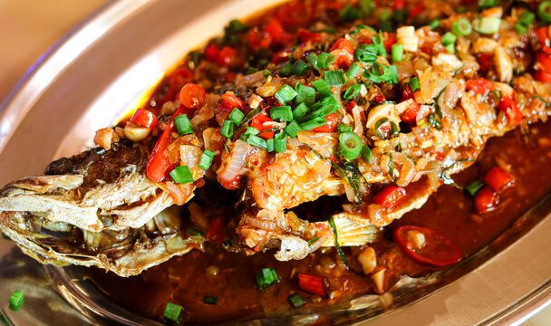 A mouth-watering whole fried fish, covered in a rich and spicy chili sambal gravy, garnished with fresh chopped green onions.