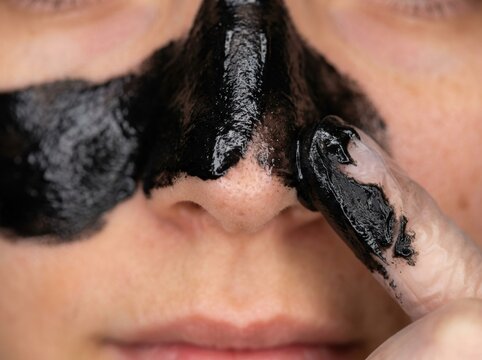 Woman applying black charcoal facial mask on nose for deep pore cleansing