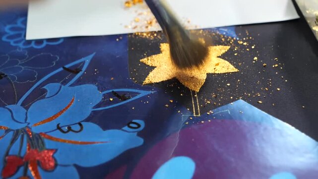 Brush continues applying gold powder onto a star shaped stencil area with scattered gold flakes