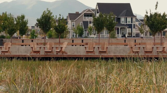 Rows of wooden chairs sit along a boardwalk facing marsh grass and homes