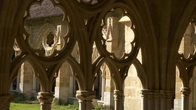 Intricate gothic stone tracery windows looking into the courtyard of the Bayonne Cathedral cloister, focused on architectural detail.