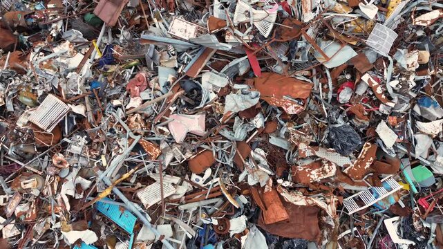 A cinematic horizontal drone fly-backward and rising top-down shot, starting from close-up textures to reveal a massive circular mountain pile of industrial scrap metal inside a recycling yard.