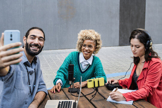 Diverse hosts recording podcast interview outdoors - Friends doing selfie picture during live stream show