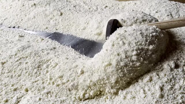 Slow motion close up shot of traditional cassava flour processing and roasting with a wooden tool in Brazil