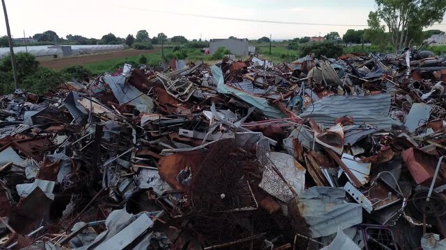 A horizontal drone cinematic shot rising high and tilting down to transition into a perfect top-down view, revealing the massive abstract texture of an industrial scrap metal recycling pile.
