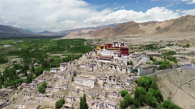 Cinematic drone slow arc shot orbiting the tiered architecture of Thiksey Buddhist Monastery built on a rocky hill, revealing a lush green valley and barren mountains in Leh Ladakh, India.