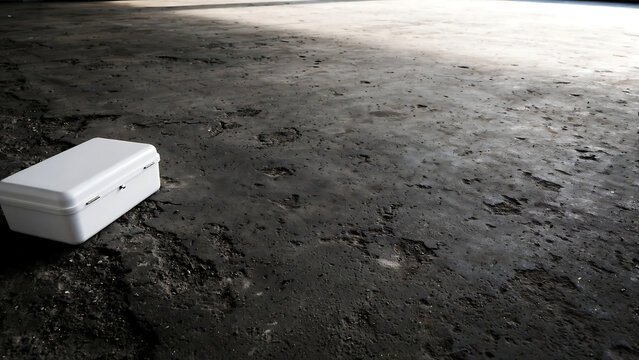 A solitary white rectangular plastic container sitting on a dark textured grey concrete floor background