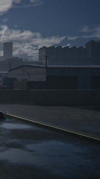 The scene shows a city street with a wet pavement. Buildings rise in the background. The sky is cloudy, and the sun is low, creating a moody atmosphere in the evening.