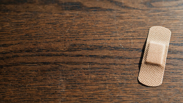 Single adhesive bandage plaster for first aid and wound protection on a dark wooden texture background