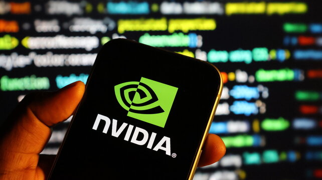 Closeup of a hand holding a smartphone displaying the nvidia logo with computer code in the background