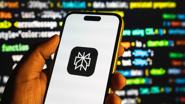 Hand holding a smartphone displaying the logo of the social media platform artifact against a background of computer code