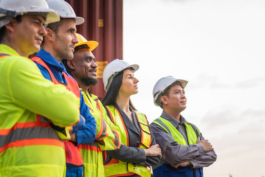 Group of international logistics professionals standing with arms crossed at shipping yard, Diverse team of logistics workers and engineers standing together at cargo terminal