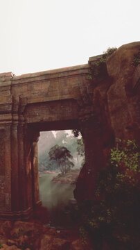 A large stone bridge stands over a waterway surrounded by rocks and trees. Mist hangs in the air, adding to the nature scene. The structure shows signs of age and history.