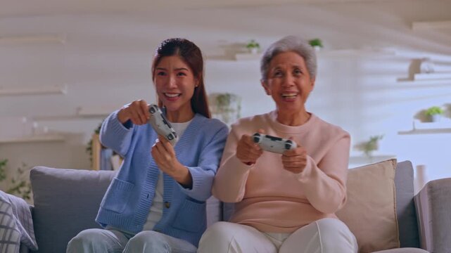Young woman senior smiling while playing video game controller on couch, cheerful family leisure at home with cozy living room technology together