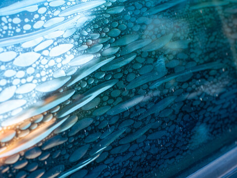 Air bubbles trapped in old deteriorated car window tint film, damaged adhesive layer on glass surface with peeling texture, vehicle maintenance problem and poor installation concept