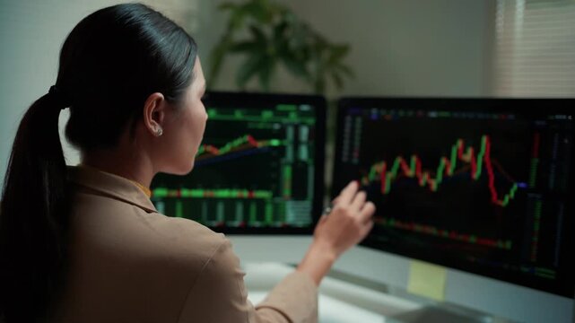 Businesswoman monitoring financial trading data on computer screens. A female broker analyzes stock market trends and forex graphs for investment