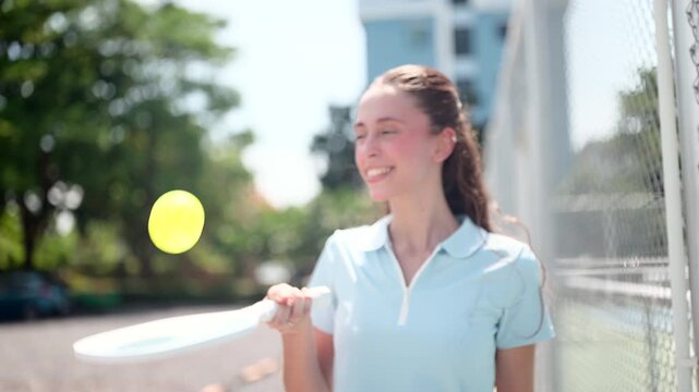 An active, confident, athletic woman, vibrant and cheerful, in her workout attire, practicing pickleball on the sidelines to warm up before a match..
