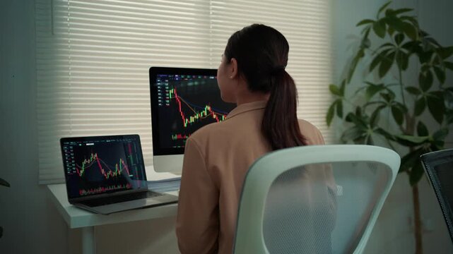 Young businesswoman working on her computer, monitoring crypto price charts. Successful female trader analyzing financial data at her desk