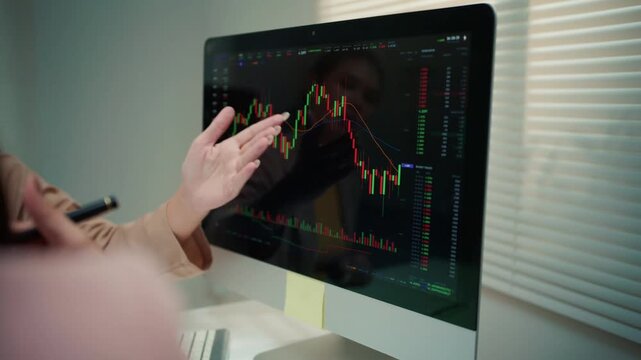 Businesswoman's hand pointing at a candlestick chart on a computer screen. Financial expert analyzing a bearish market and a price fall