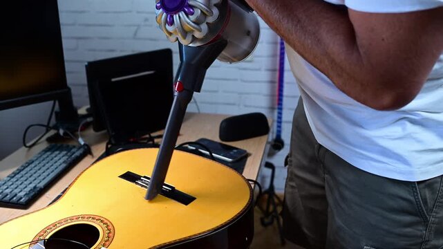 Person vacuuming an acoustic guitar with a cordless vacuum cleaner
