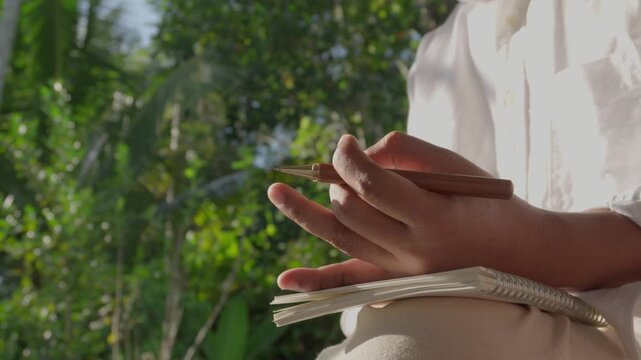 Mindful pause leading to creative inspiration as a person gently reflects before writing ideas in notebook outdoors, promoting mental clarity, focus, productivity, creativity, and intentional thinking