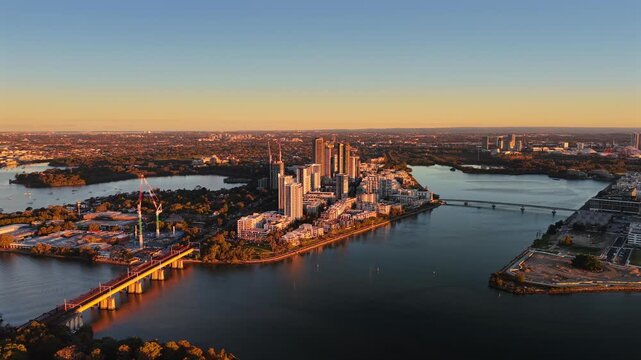 Aerial drone video over Rhodes, Sydney, from the north side, showing surrounding suburbs, waterways, land, and modern residential development.