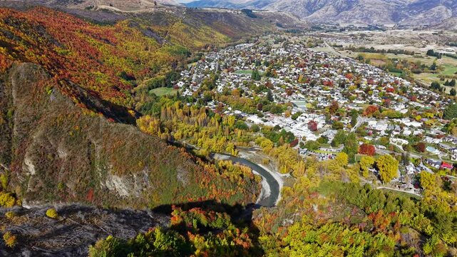 Aerial drone video rotating over Arrowtown, New Zealand, showing the historic South Island town, surrounding hills, streets, trees, and scenic mountain landscape.