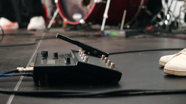 Close-up of a guitarist controlling an effects pedal with a foot during a live concert. Professional stage equipment, guitar effects processor and performance technology in action.