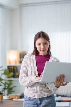 Young Asian woman student using laptop for online learning in bright modern home office with copy space