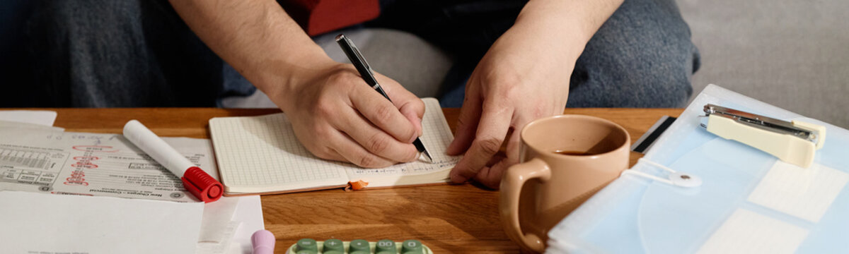 Close up of young adult man writing notes in planner beside bills and calculator, managing household budget and expenses. Ideal for personal finance, debt planning, budgeting content