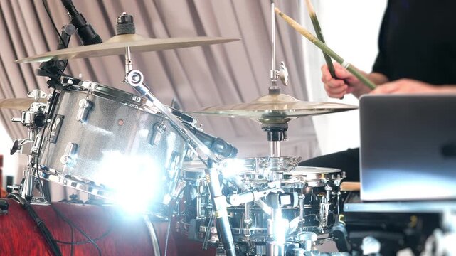 Professional drummer performing on a modern drum kit with microphones during a live concert or rehearsal. Close-up of percussion instruments in an energetic music performance setting.