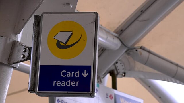 Static close-up of a contactless card reader sign hanging from metal beams at a public transport station.