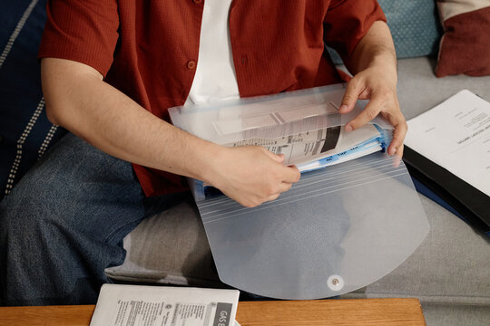 Close up of young adult man organizing bills and paperwork in plastic folder at home, managing household finances and records. Useful for budgeting, taxes, insurance, admin