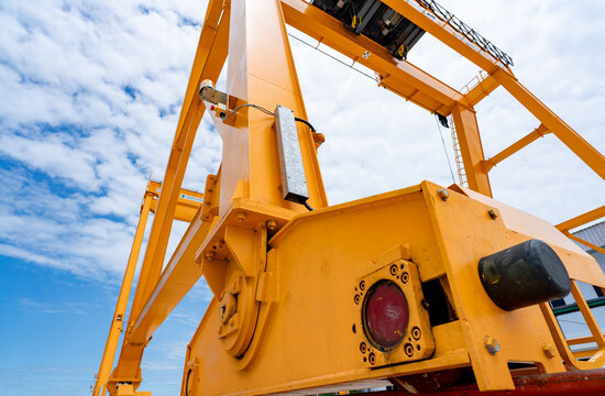Bottom view of yellow gantry crane against blue sky at port. Gantry crane for cargo and construction industry. Overhead crane for lifting heavy loads. Safety and security working on gantry cranes.