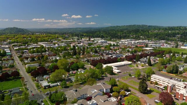 Wide aerial view above downtown neighborhoods with tree lined streets and forested hills